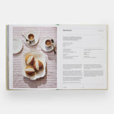 Calimia Home The Regional Italian Cookbook book open to a spread showing a sweet bun recipe on a striped tablecloth.
