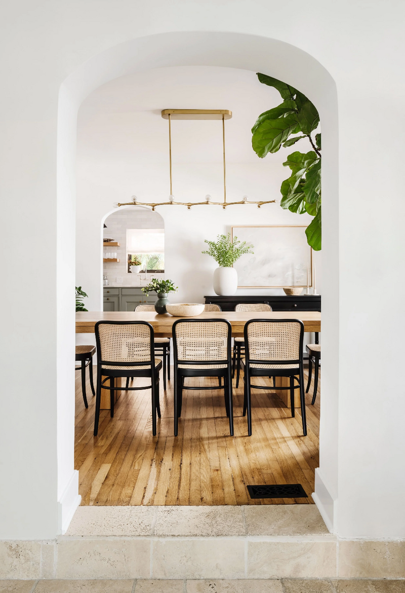 Arched doorway opening to a dining room with cane-back chairs in the Spanish in the Gables remodel