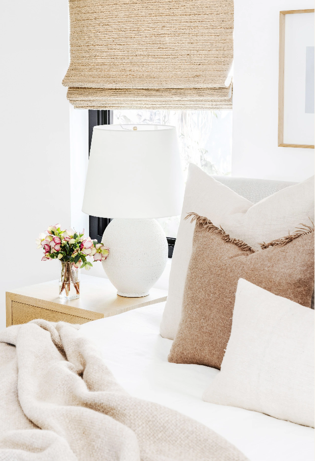 Bedside styling with a white ceramic lamp, fresh flowers, and textured linen pillows
