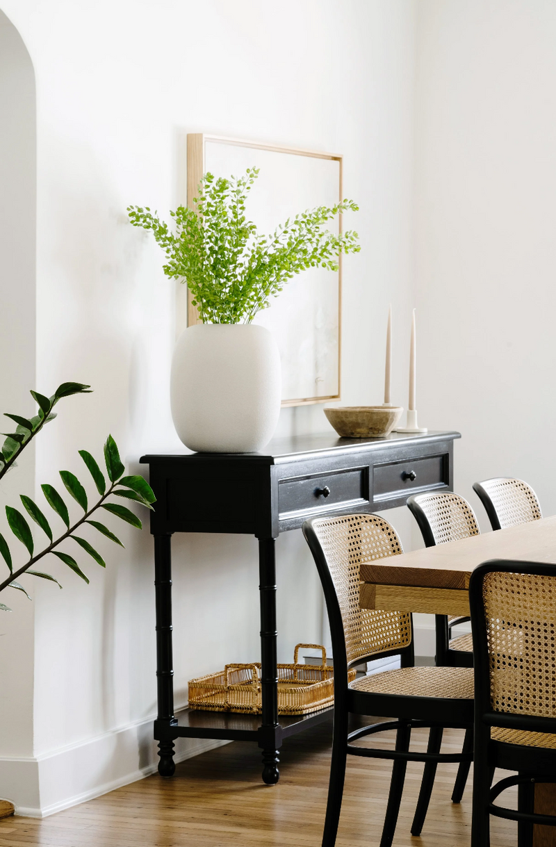 Black console table styled with a white vase of maidenhair fern beside the dining table