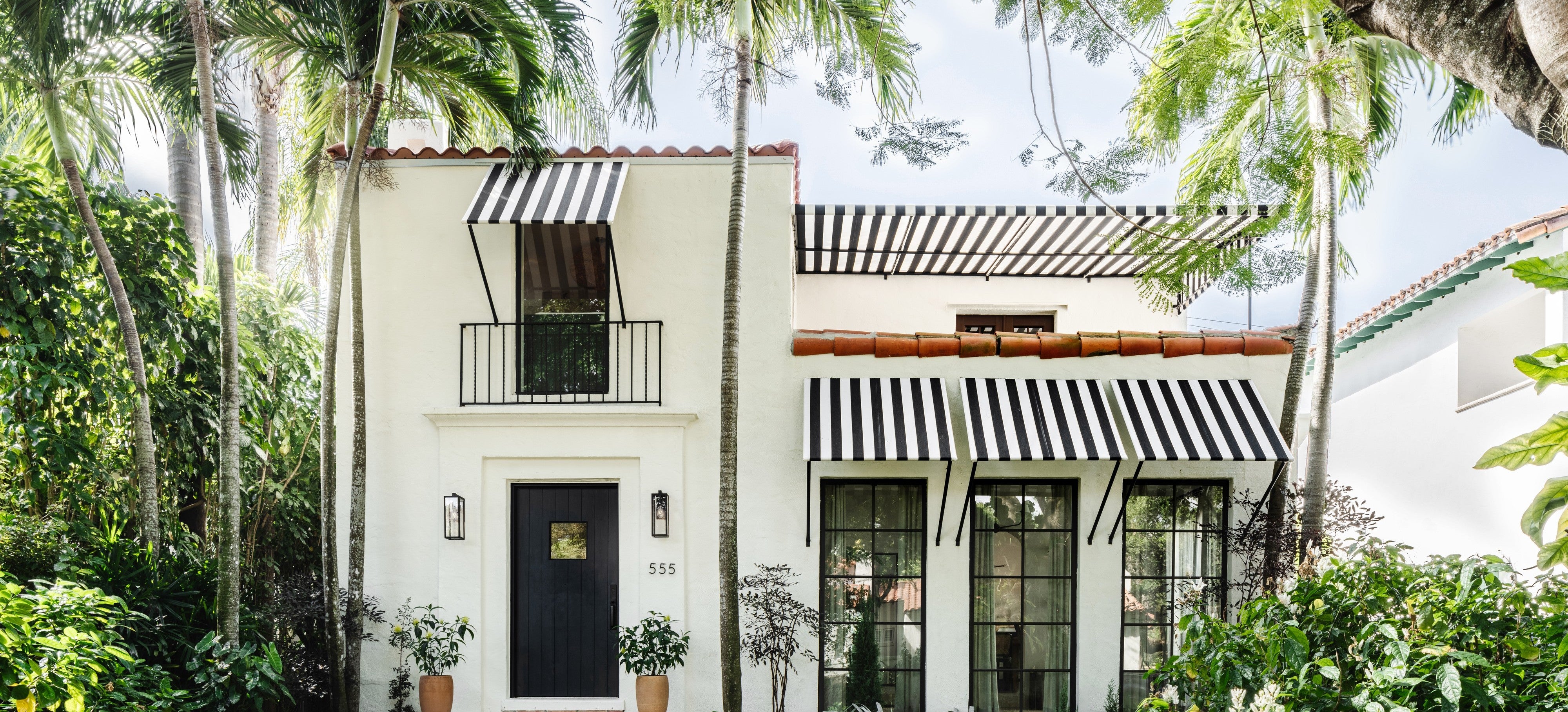 White Spanish-style home with black and white striped awnings framed by palms in Coral Gables