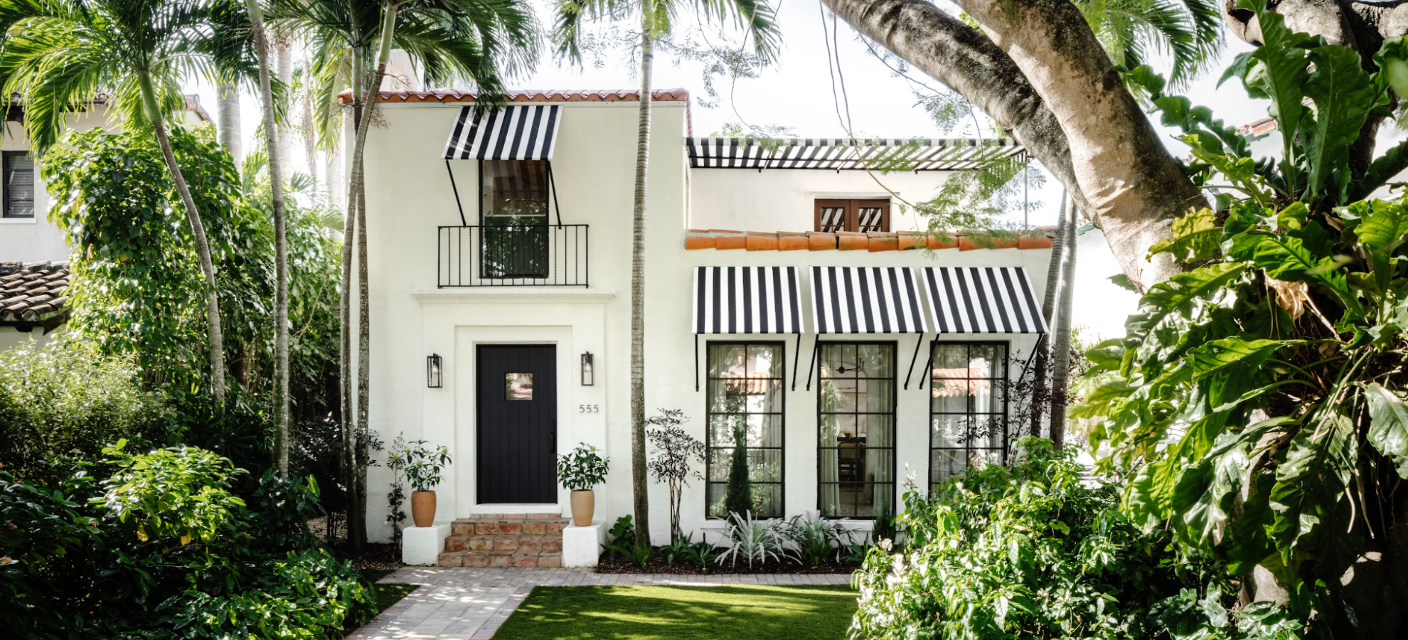 White Spanish-style home with black and white striped awnings framed by palms in Coral Gables