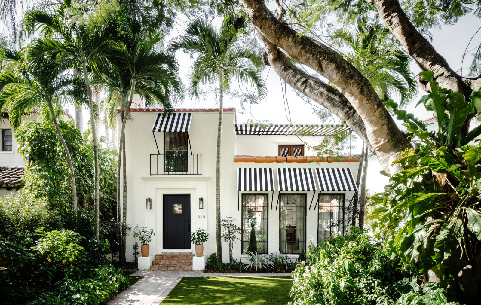 Striped awnings and tropical plantings on a restored Spanish home facade in Coral Gables, Florida