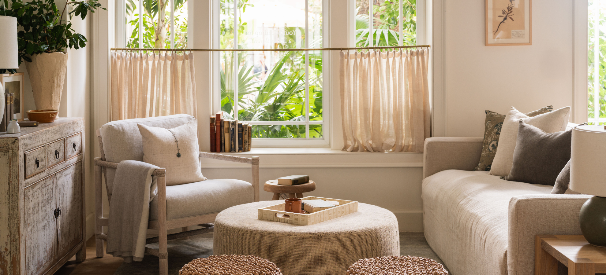Sunlit sitting room with neutral armchairs and woven ottoman, designed by Calimia Home's Coral Gables studio