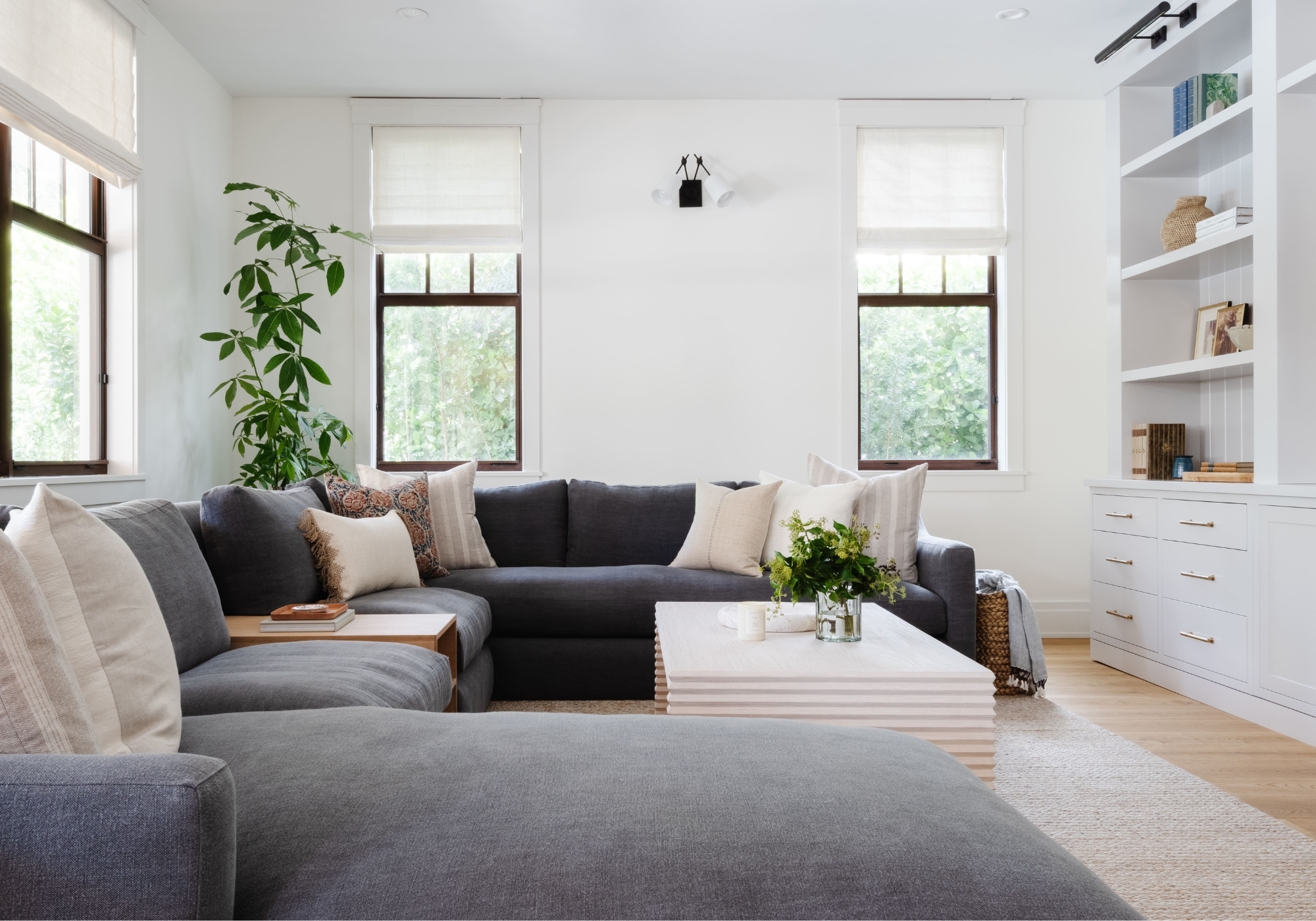 Bright living room with gray sectional and built-in shelving, room design by Calimia Home in Coral Gables