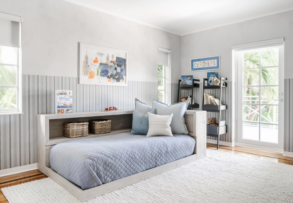 Boy's room with upholstered daybed, striped paneling, and picture-ledge shelving in soft blue tones