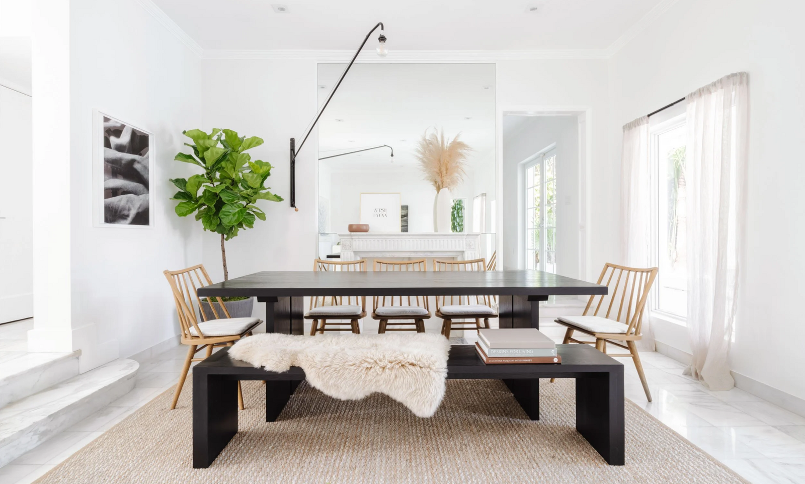 Minimal dining room with black table, woven chairs, and layered rugs beneath a sculptural light