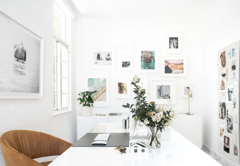 Bright home office with gallery wall, white desk, and cognac leather chair designed by Calimia Home