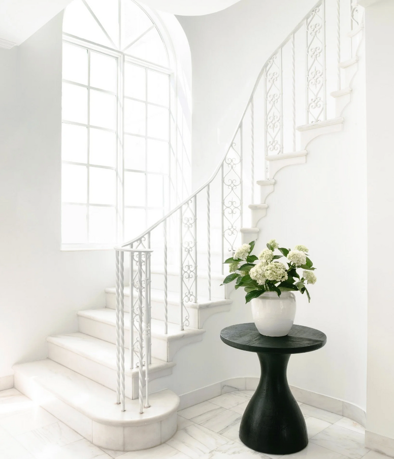 Sweeping white spiral staircase with black pedestal table and fresh hydrangeas, Miami Beach