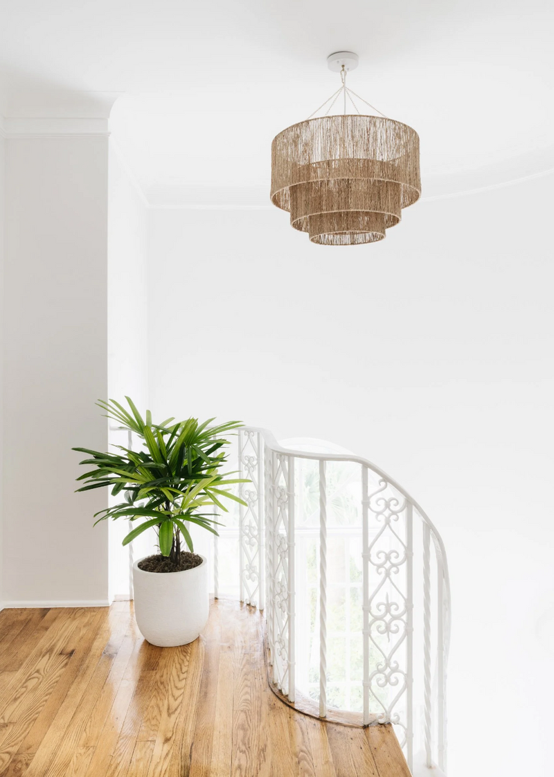 Tiered jute pendant above a stair landing with ornate white ironwork and a potted palm