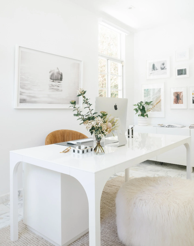 All-white office with arched desk, fresh flowers, and a plush sheepskin stool