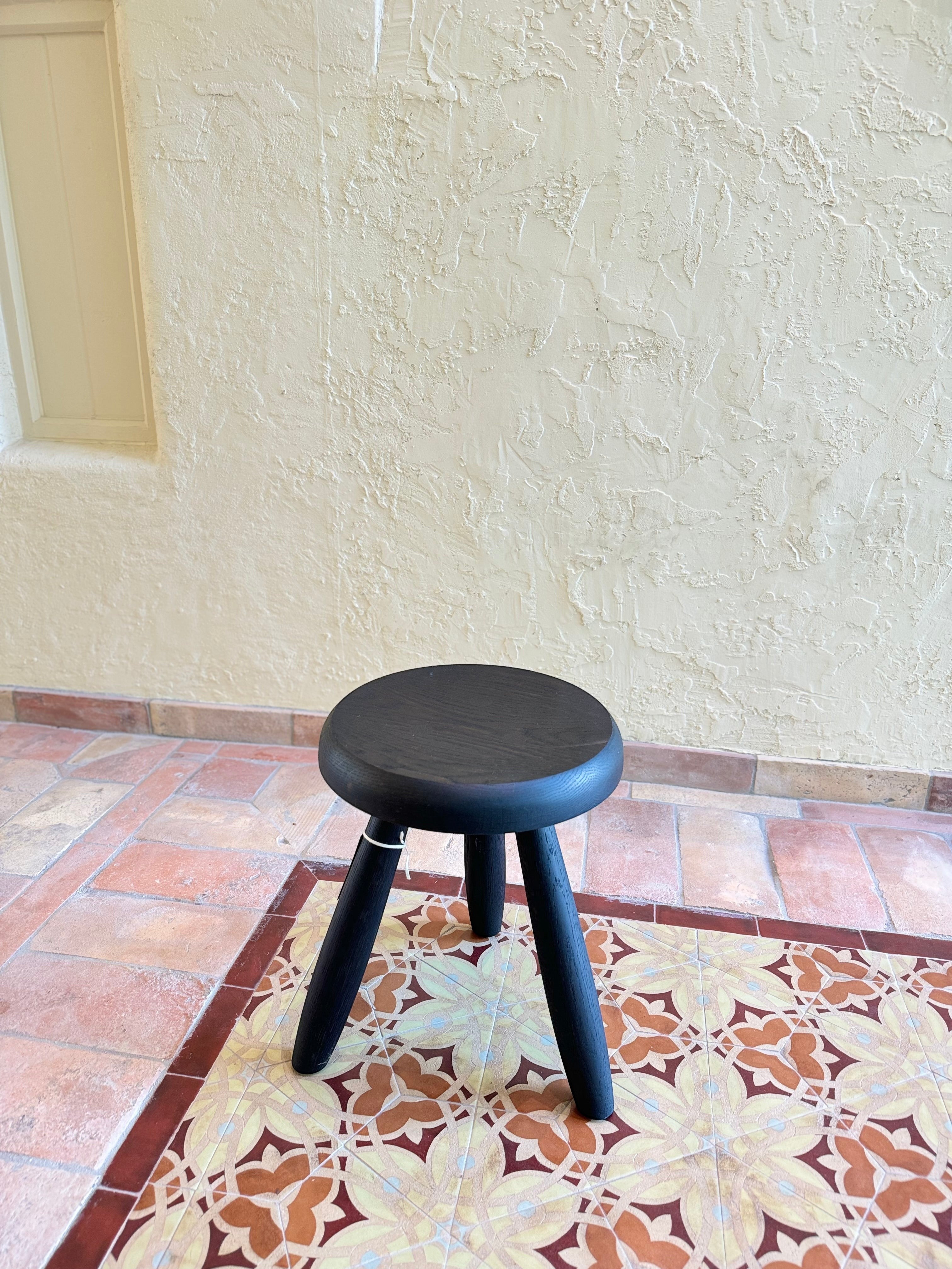 Calimia Home Tori Stool in black wood with three tapered legs and a round seat on a patterned tile floor.