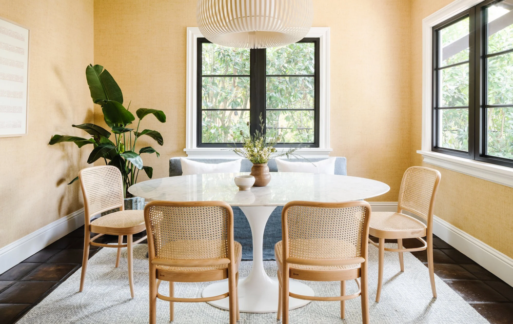 Dining room with a round table and wicker chairs in a well-lit room.