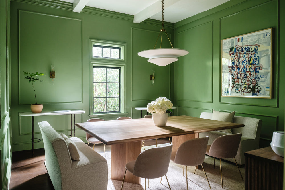 Green-paneled dining room with oval wood table and sculptural pendant, designed by Calimia Home