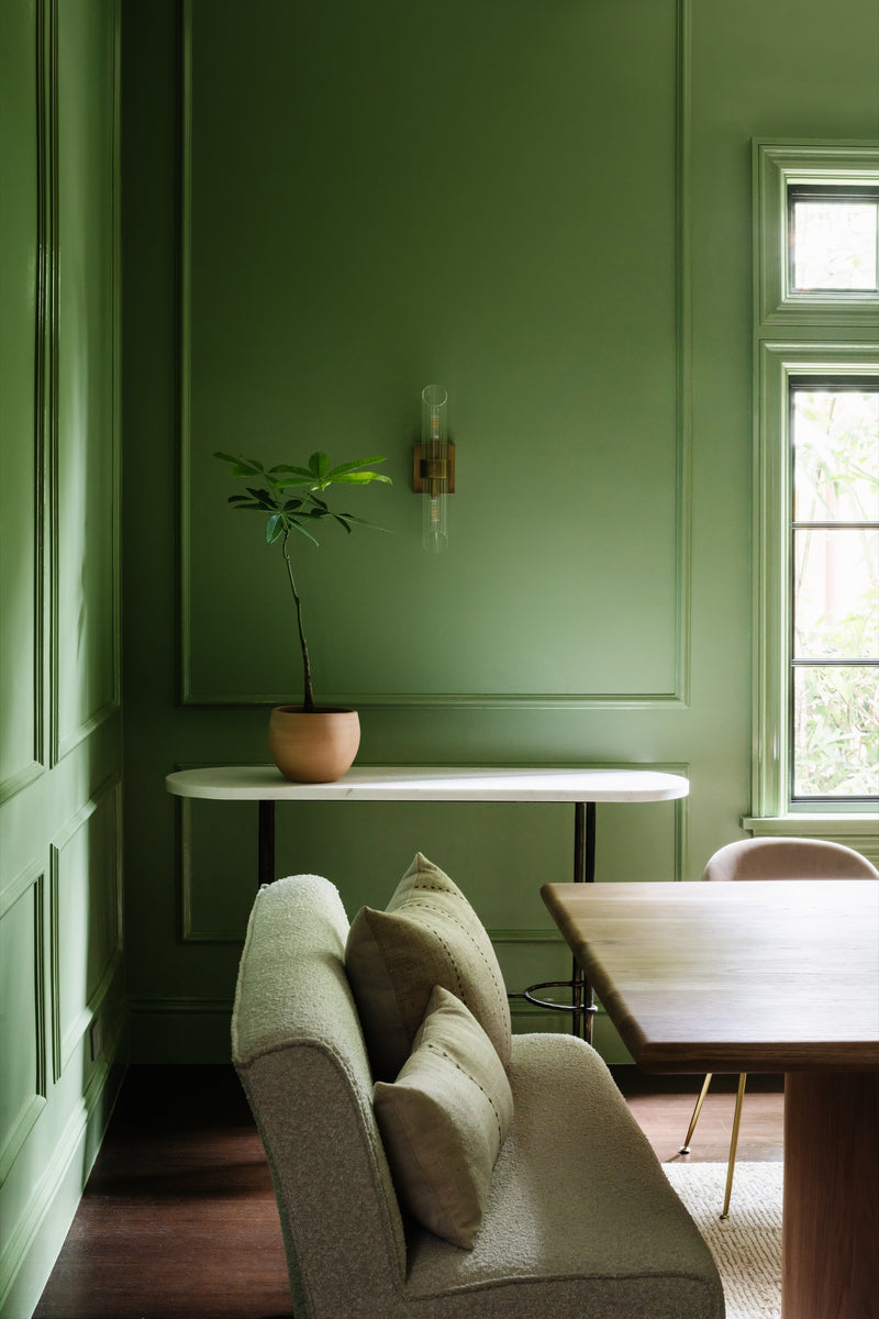 Dining room corner with green paneling, marble-top console, brass sconce, and potted plant