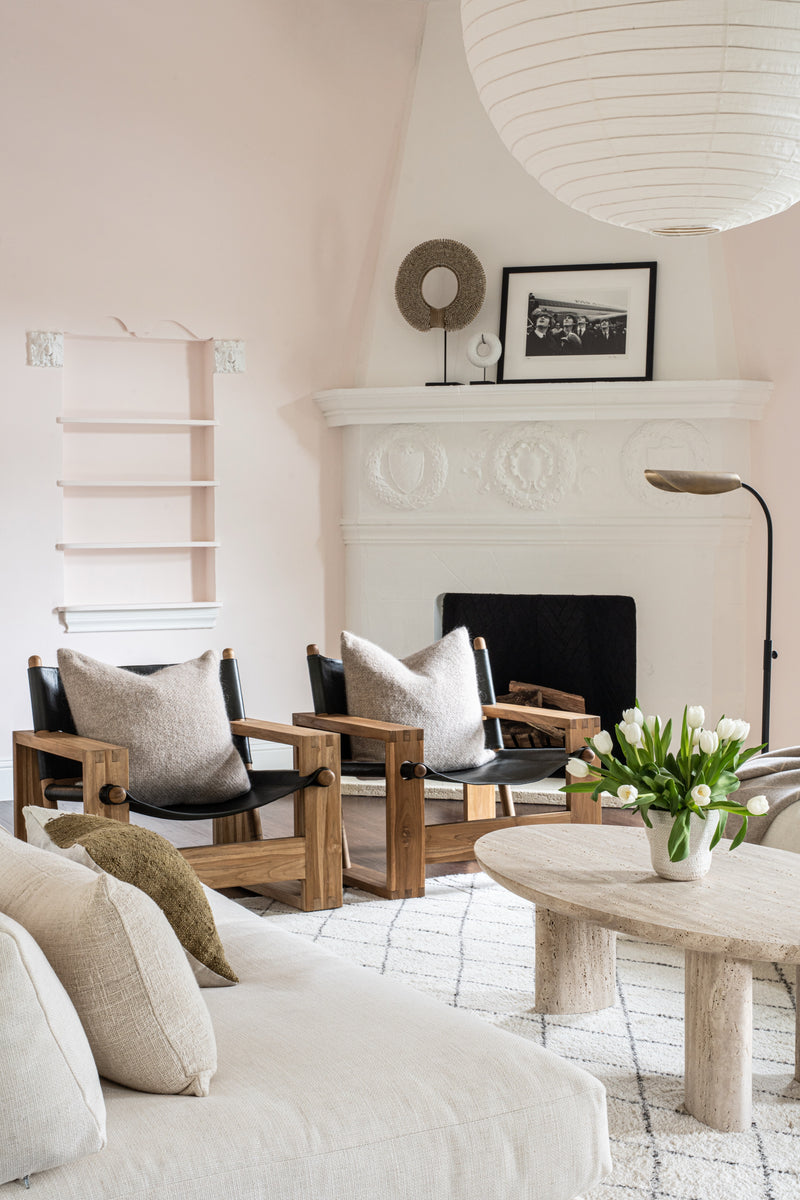 Sitting area with carved plaster fireplace, black wood lounge chairs, and travertine coffee table