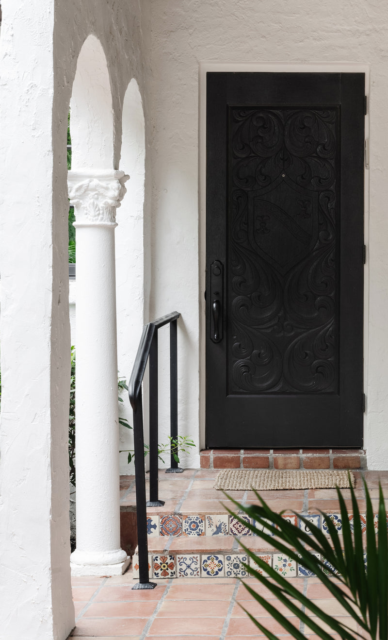 Carved black front door framed by arched white columns and patterned tile at Villa Belmonte, West Palm Beach