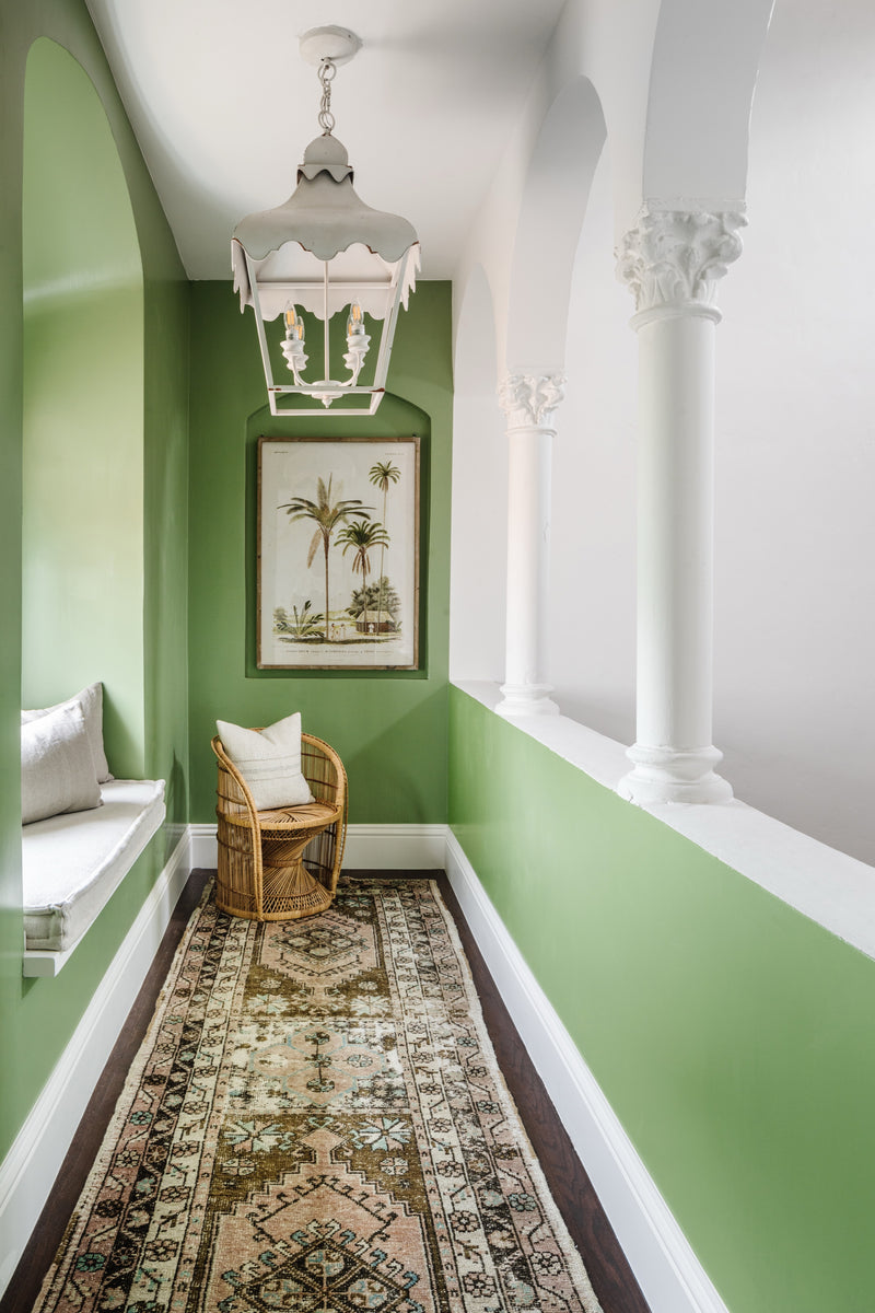 Green loggia with white pagoda lantern, palm print art, rattan chair, and vintage runner