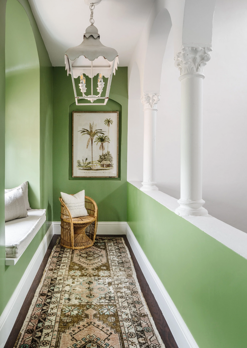 Green loggia with white pagoda lantern, palm print art, rattan chair, and vintage runner
