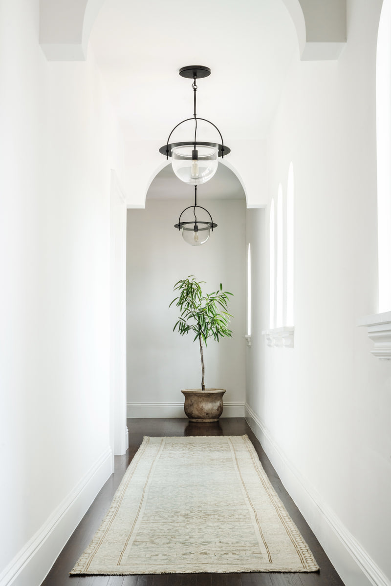 Arched white hallway with glass globe pendants, potted plant, and vintage runner at Villa Belmonte