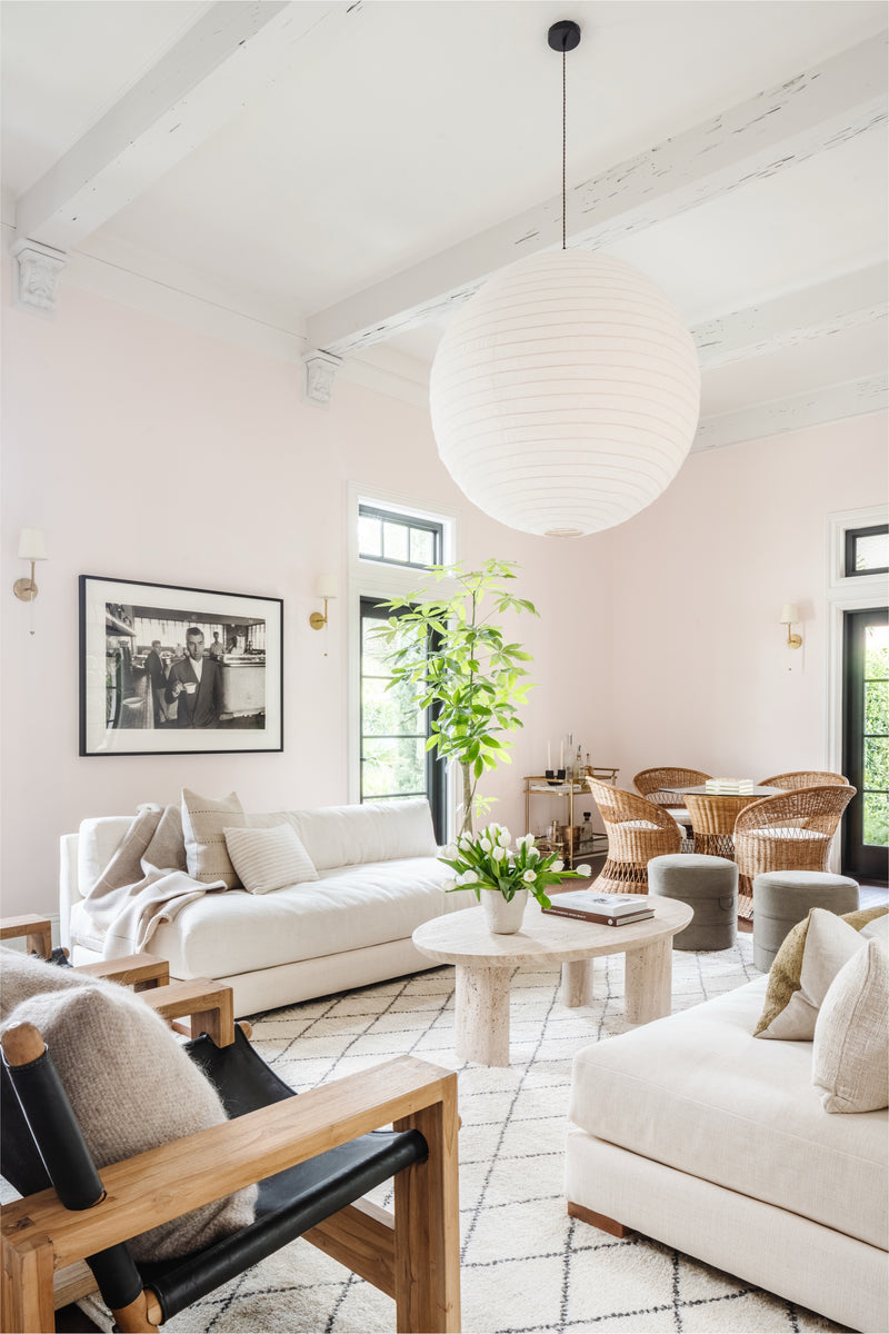 Living room with white sofas, round paper lantern, and rattan dining chairs beyond