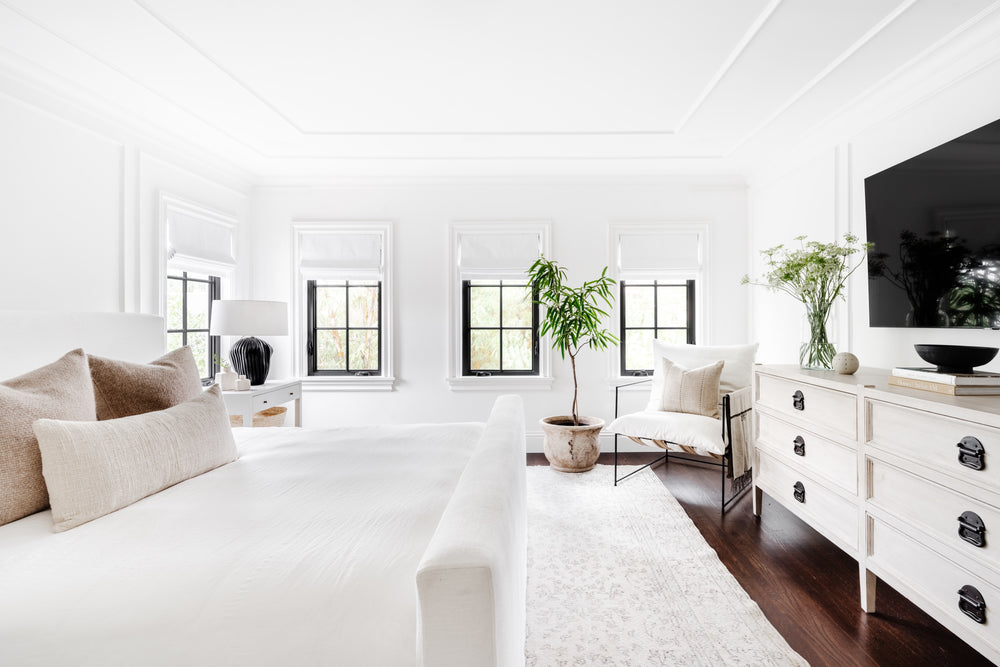 Primary bedroom with crisp white bedding, paneled walls, and black-framed windows