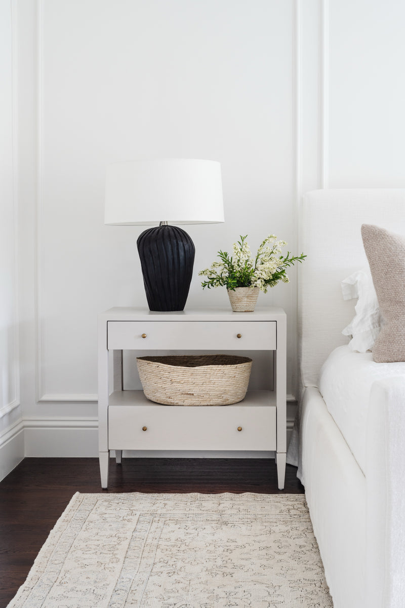 Grey nightstand styled with a black lamp, fresh flowers, and a woven basket