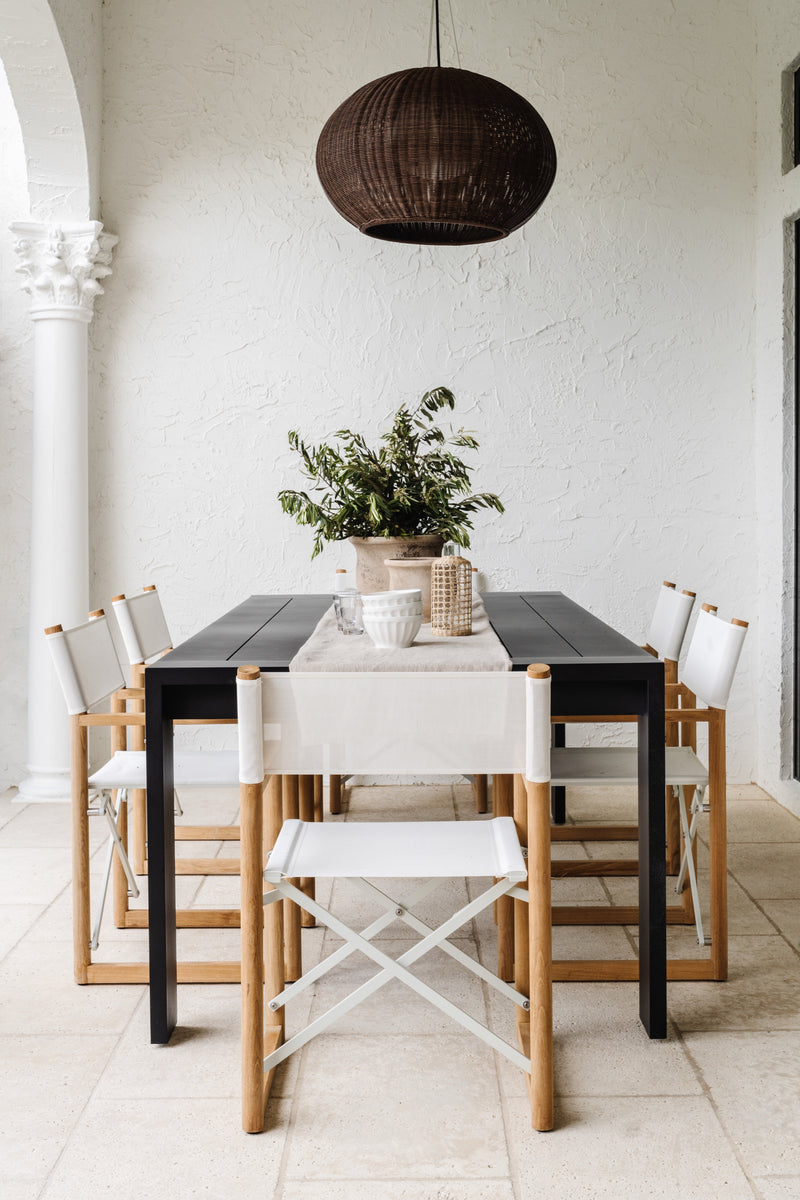 Outdoor dining area with black table, white sling chairs, and woven pendant at Villa Belmonte