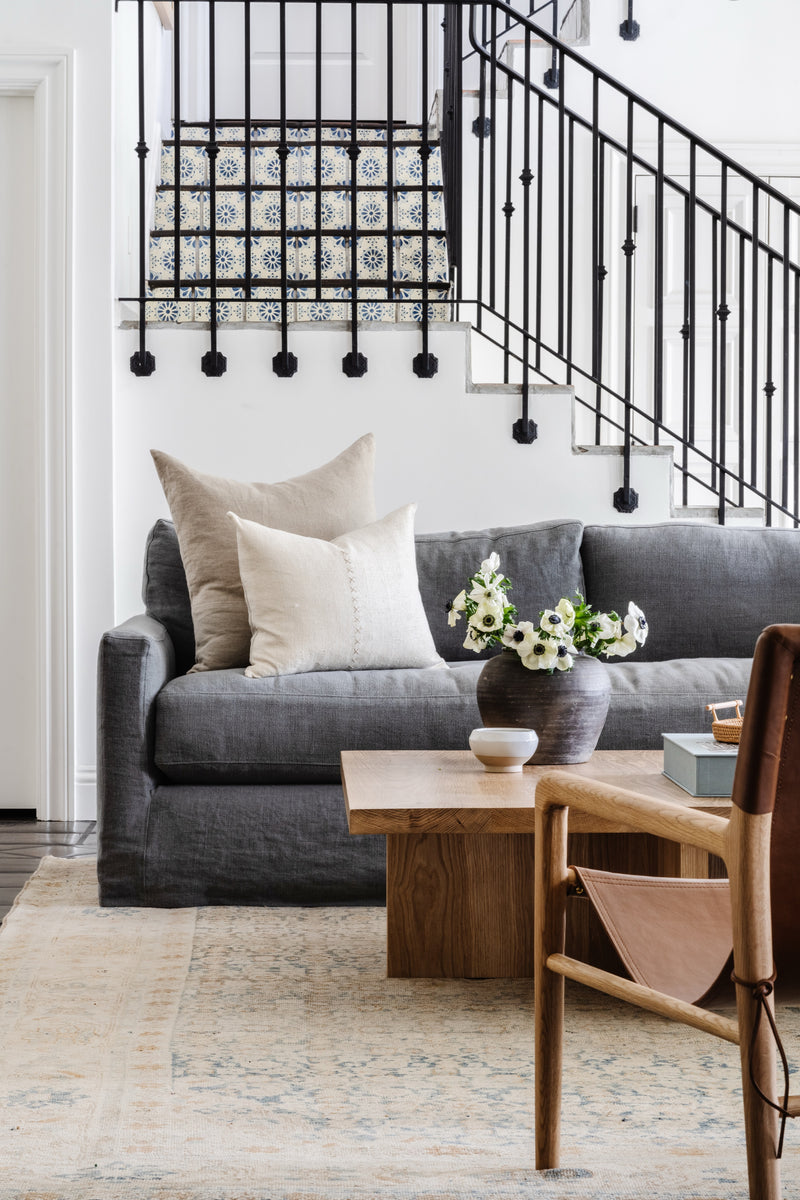 Charcoal slipcovered sofa beneath a wrought iron stair railing with a leather sling chair