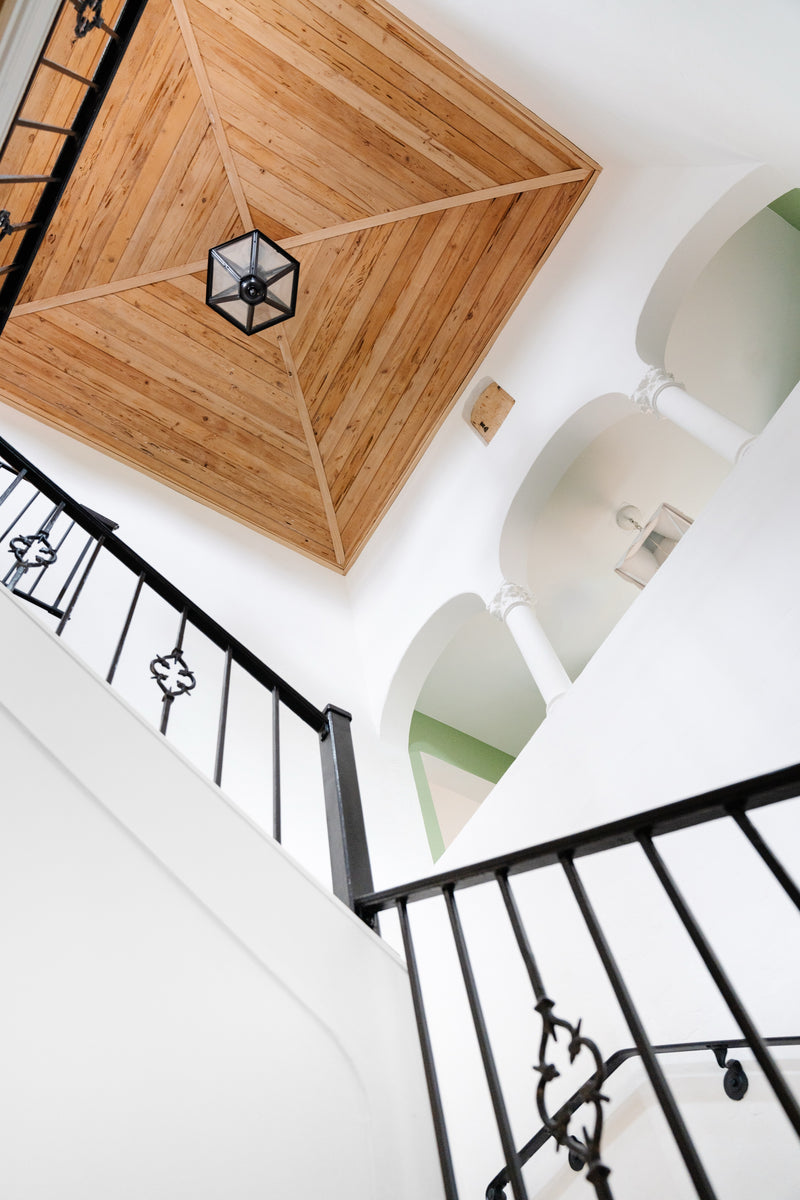 Looking up a stairwell at a wood-paneled ceiling, lantern pendant, and wrought iron railing