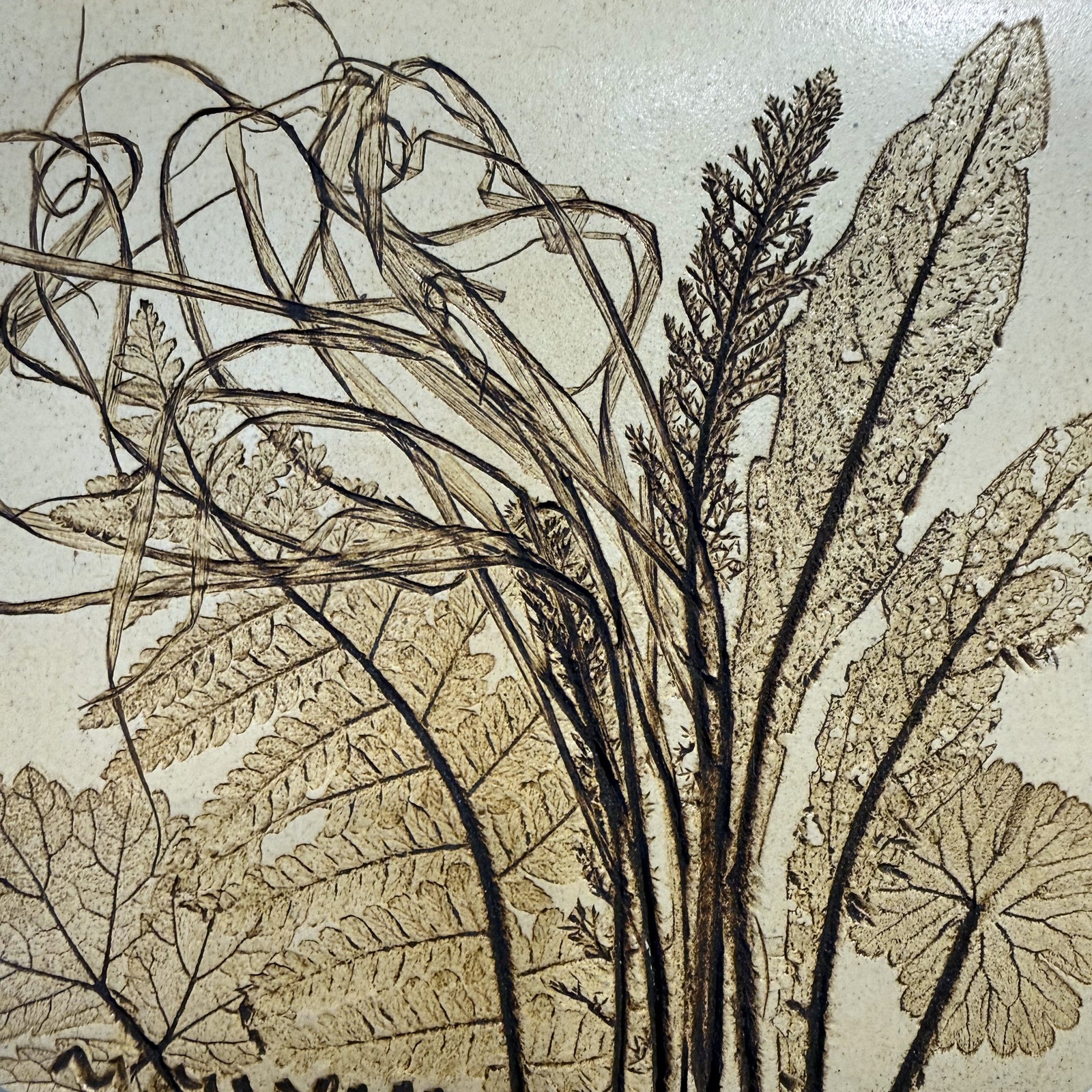 Close-up of a vintage ceramic botanical wall tile showing the deep relief texture of fern and dock leaf impressions