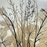 Close-up of a vintage ceramic botanical wall tile showing grass seed heads and leaf veins pressed in relief with an iron-toned wash