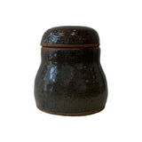 Studio pottery lidded jar in mottled near-black glaze with domed lid and bands of bare reddish clay at the foot and rim