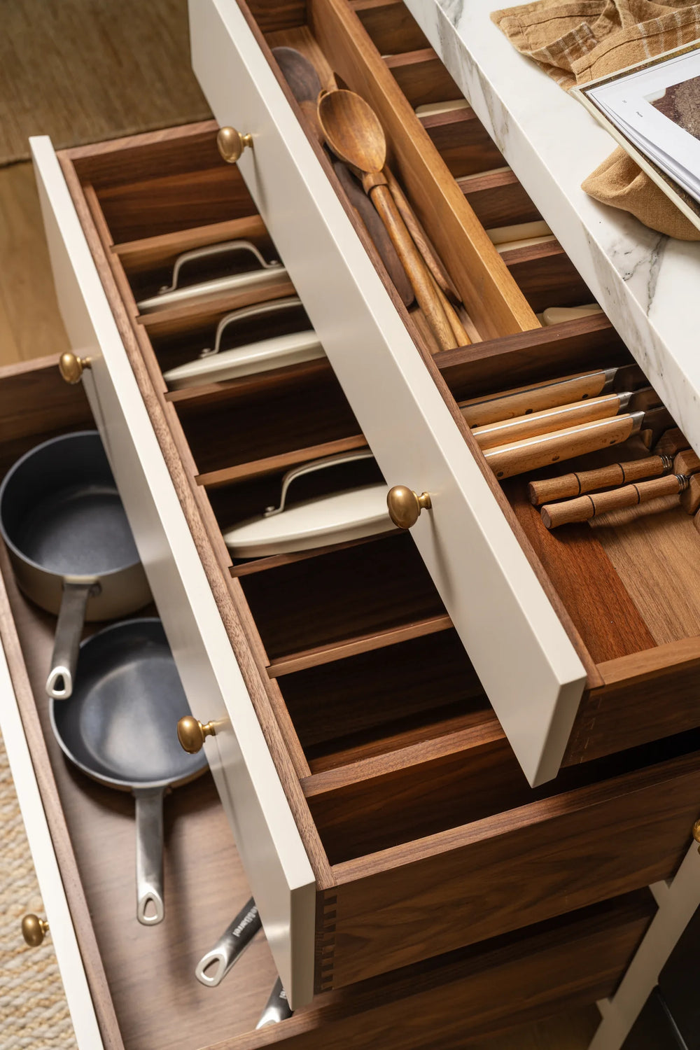 Open walnut drawers with dovetail joinery and organizers for utensils and pans in custom cream cabinetry