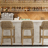 Calimia Home Capitola bar stools with natural pole rattan frames, woven seagrass, and antique brass footrests at a bar.