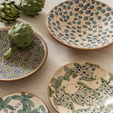 Calimia Home handcrafted ceramic plates with hand-painted fish, cherry, and palm tree motifs on a marble surface.