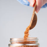 Calicutts Chipotle and Honey spice blend being poured from a wooden spoon into a glass jar.