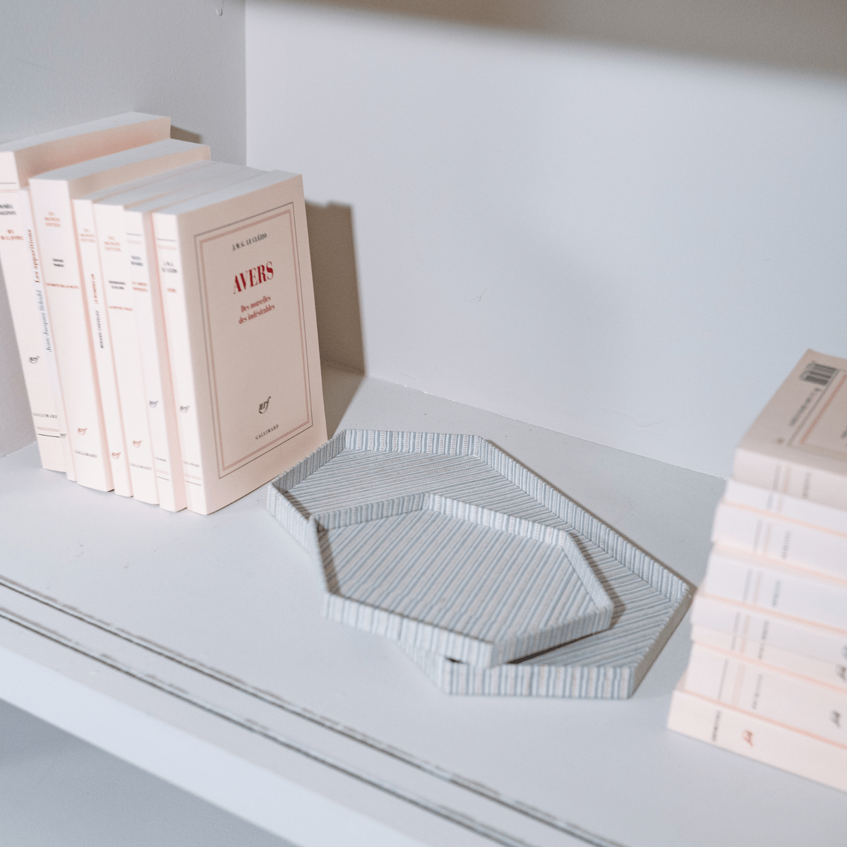 Clémence hexagon trays in Blue Mist stripe styled on a white bookshelf beside stacked books