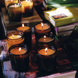 Flamingo Estate Climbing Tuscan Rosemary candles in forest-green glass jars, hand-poured soy wax glowing on stacked books.