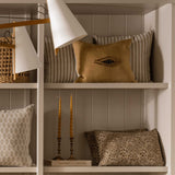 Calimia Home Eira mustard linen pillow with hand-embroidered wool eye motif displayed on a white shelf
