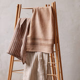 Sir Madam set of two earth-toned striped linen tea towels draped over a wooden ladder rack.
