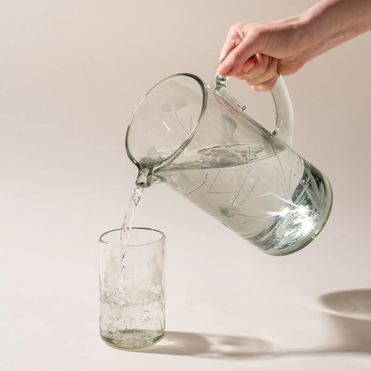 Hand-blown glass pitcher shown from the side with visible etched design