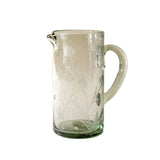 Clear glass pitcher with floral etching on a beige background