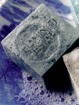 A lathered Flamingo Estate Peppermint Bar tilts on a blue and white china plate, frothy bubbles obscuring its embossed face in a moody close-up.