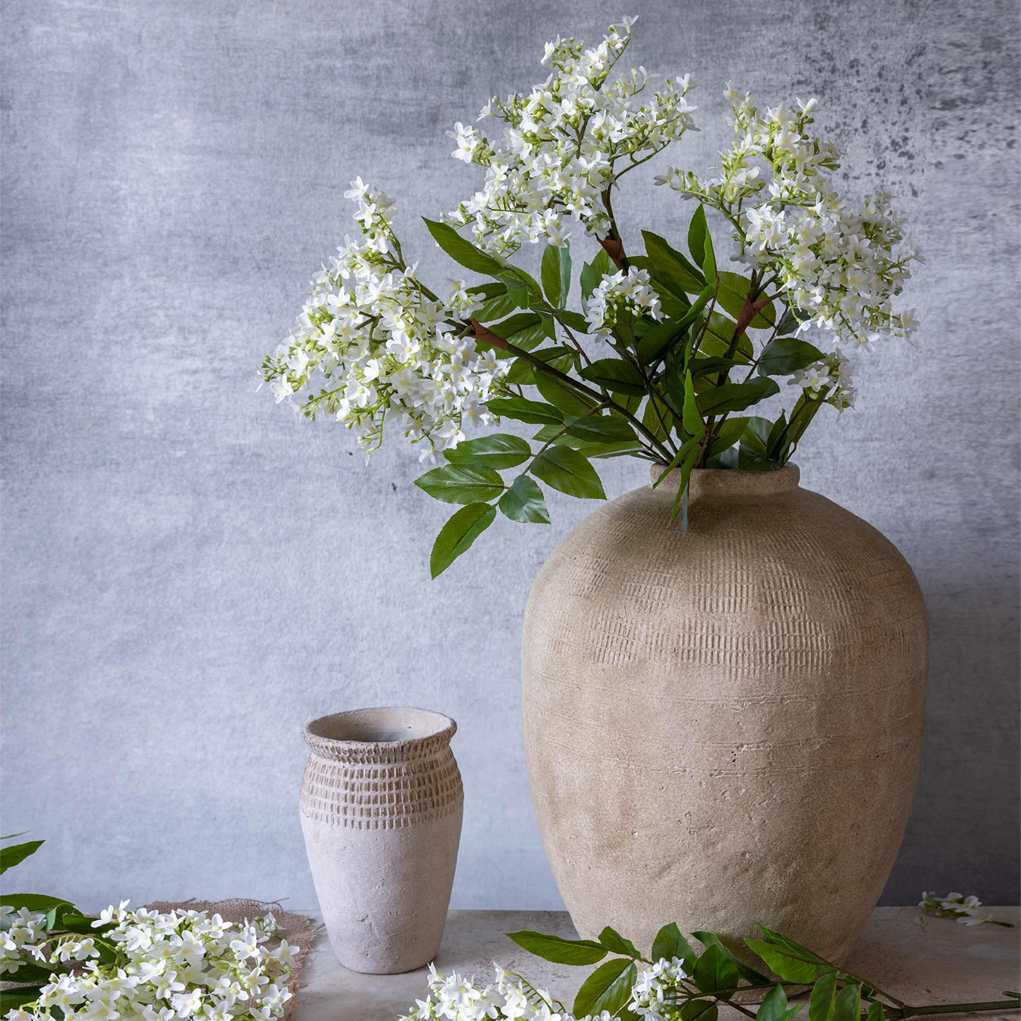 White faux lilac stems by Abigail Ahern arranged in a rustic terracotta vase, lifestyle styling shot