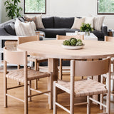 Valencia X Dining Table in natural oak by Grove & Anchor, styled with woven-seat dining chairs beside a living area, exclusive to Calimia Home