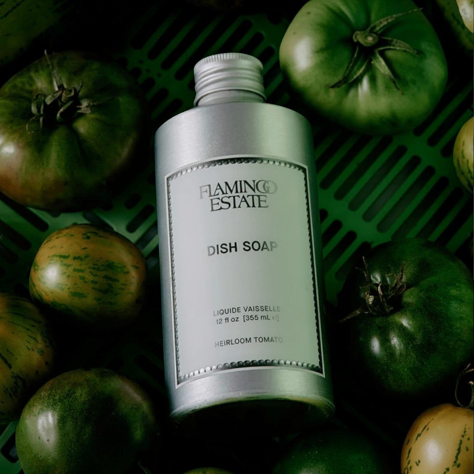 Flamingo Estate Heirloom Tomato dish soap in a refillable aluminum bottle surrounded by fresh green tomatoes.