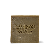 The olive-green Flamingo Estate Rosemary & Parsley Soap Brick, flecked with herbs and embossed with the brand wordmark, on a white background.