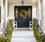 28-inch fresh magnolia wreath on a black front door of a white brick porch with columns and a hanging lantern