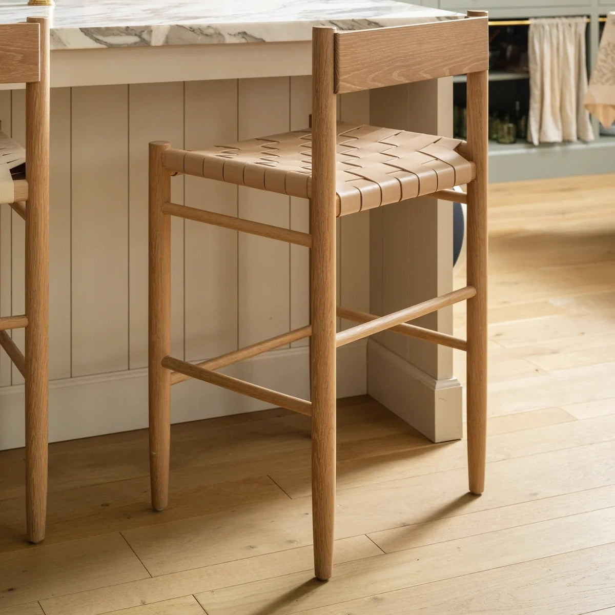 Flag Counter Stool in white oak and woven natural leather pulled up to the marble kitchen island